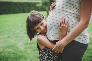 child girl 5 years old hugs mother's pregnant belly in the park in nature in summer