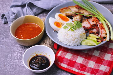 rice with red pork on top served with boiled egg, cucumber and crispy pork with dipping sauce and soy sauce served in the restaurant