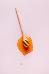 top view of wooden honey spoon with spilled honey on pink background