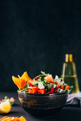 close-up on a bowl with vegetable salad on a background of lemon and a bottle of olive oil on a dark background