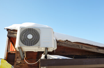 Snow covered invertor Air conditioner outdoor unit closeup on roof top. A snow-covered roof of a...