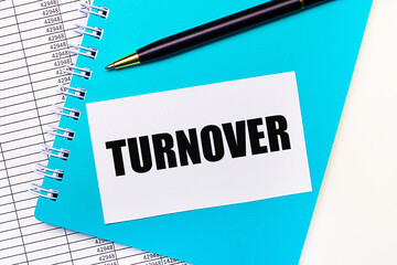 On the office desk there are reports, a blue notepad, a black pen, and a white card with the text TURNOVER. Stylish workplace. Business concept
