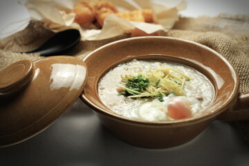 Hot Chinese pork congee top with soft boiled eggs served in a Chinese style clay pot with deep fried dough stick for breakfast. Rice soup concept.