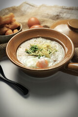 Hot Chinese pork congee top with soft boiled eggs served in a Chinese style clay pot with deep fried dough stick for breakfast. Rice soup concept.