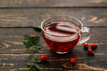A cup of rose hip tea with fresh berries in a glass cup on dark wood background. Vintage background, selective focus