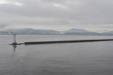 Lighthouse in an ocean bay on a foggy, misty and cloudy grey seascape with horizon at the sea or ocean in Asia