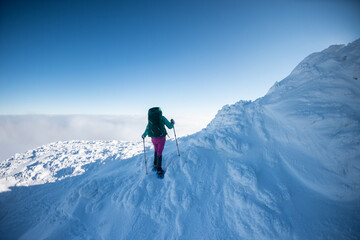 Fototapeta na wymiar A woman with a backpack in snowshoes climbs a snowy mountain