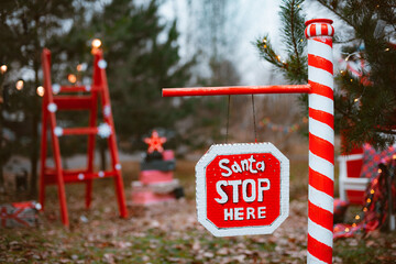 Outdoor road barrier in Christmas decorations in pine trees with the inscription Santa, please stop here.