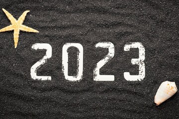 Concept de bonne année 2023 avec un coquillage et une étoile de mer sur du sable de plage noir....