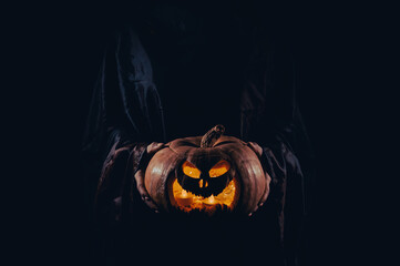The witch is holding a pumpkin jack o lantern glowing in the dark. Halloween.