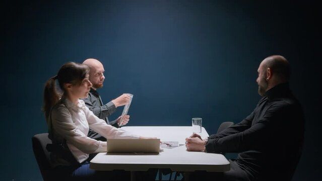 Two detective cops interrogate murder suspect. Police officer shows knife in blood in Evidence bag. Female FBI agent shows handcuffed criminal photo from crime scene. Russian mafia denies all charges