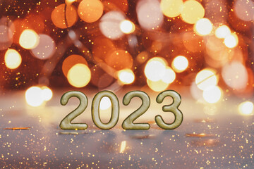 Golden numbers of year 2023. Happy New Year greeting card. Glowing festive garland with bokeh on dark orange background.