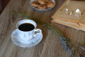 Cup of tea, plate with chocolate chip cookies, open book, reading glasses, lit candles and dry lavender flowers. Hygge at home, selective focus.