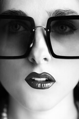 Fashion, make-up and style concept. Close-up beautiful and young woman retro portrait with big sunglasses and make-up looking to camera. Selective focus. Nose in camera focus. Black and white image