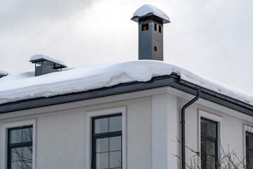 Corner of house with new roof made of gray metal tiles and gutter with metal smoke pipe covered with thick layer of snow in winter. Metal Downpipe system, Guttering System, External downpipes