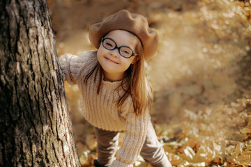 Cute little girl with a health disorder in a knitted sweater and hat and stylish glasses peeks out...
