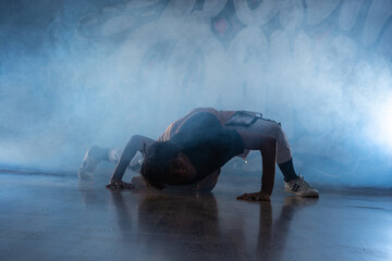 Young man break dancing in club with lights and smoke.