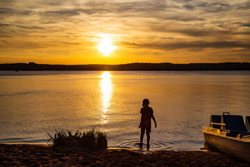 Chłopiec w wodzie przy zachodzie słońca nad Zalewem Sulejowskim. 