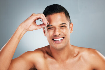 Portrait of a man tweezing his eyebrow with a tweezer in studio with gray background. Happy, smile and young guy plucking brow for hair removal for grooming, cleaning and hygiene routine or self care