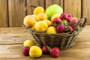 Fresh apricots strawberries and apple in the basket on wooden background