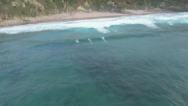 Aerial drone shot approaching a group of surfers enjoying a recreational afternoon riding the waves at Playa de Los Locos beach, Suances, Spain