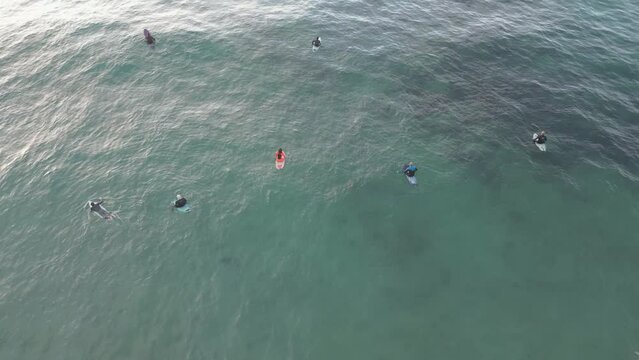Aerial drone shot tilting up to reveal a group of surfers waiting to catch the next perfect wave as the sun sets in the distance over the Cantabrian Sea, Suances, Spain