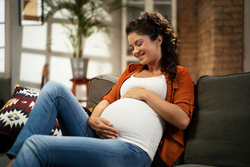 Obraz premium Pregnant woman sitting on a sofa and caressing her belly.