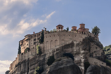 Fototapeta premium Bottom view of Varlaam Monastery, stone wall, Byzantine-style inner buildings exhibiting illustrated manuscripts in sacristy, and beautiful arched stone gazebo on panoramic terrace, Meteora, Greece
