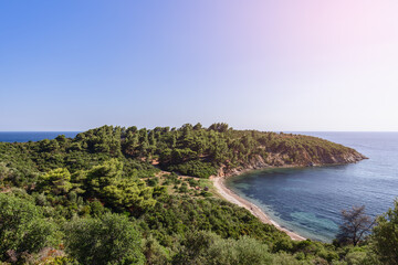 Fototapeta na wymiar Panoramic view of tiny cape, which is part of Sithonia peninsula, overgrown with dense greenery including trees, with narrow sandy beach strip, Chalkidiki, Northern Greece