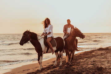 A loving couple in summer clothes riding a horse on a sandy beach at sunset. Sea and sunset in the...
