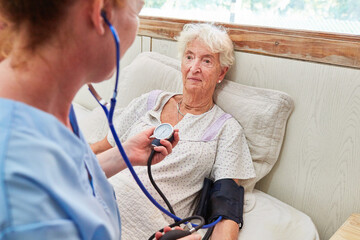 Krankenpflegerin misst Blutdruck bei einer Seniorin