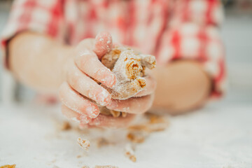 Partially blurred hands of little girl in red checkered shirt prepare dough for gingerbread cookies in white kitchen. Child knead dough on white table strewn with flour