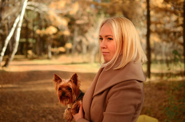A happy woman in a yellow coat with autumn leaves and a bag in her arms in an autumn yellow park. Beautiful smiling young woman in autumn foliage.