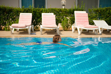 Woman in blue swimsuit swimming in the pool during hot sunny day