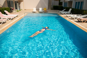 Woman in blue swimsuit swimming in the pool during hot sunny day