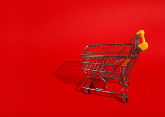 Shopping cart with shadow on red background, copy space