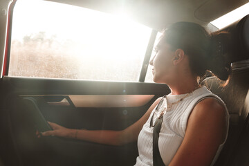 Stylish young woman sitting on back seat in the taxi car and looking through the window