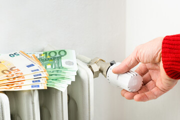 Male hand adjusting home gas heater - Euro banknotes on house radiator with man lowering the...