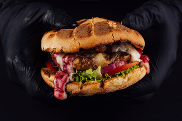 Man holds ready tasty burger in hands in black gloves
