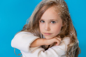 portrait of a cute little blonde girl in a white knitted sweater on a blue background in the studio. snowflakes in the hair, the concept of winter