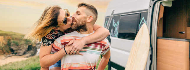 Young couple kissing piggybacking next to their camper van during a trip