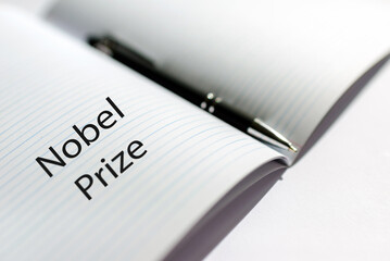 The inscription NOBEL PRIZE on a white sheet notebook.Nobel prize in literature. A pen is lying nearby.White background.Selective focus,close-up.