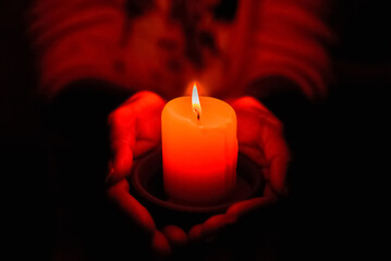 A burning candle at night,protected by the hands of a woman.Candle light glowing in woman's hands.Praying,faith,religion concept.Selective focus,closeup.