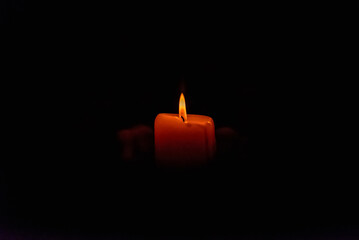 Human hands holding a burning candle in the dark. Adult woman with a red candle on the black background.Selective focus.Closeup.Copy space.