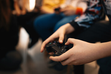 Hands of little boy playing video games at home with friends. Black gamepad in children hands
