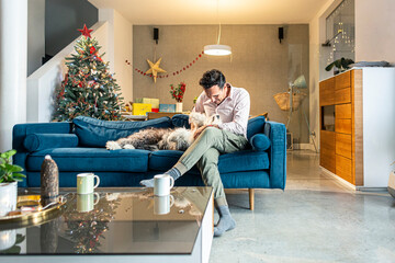 Man and his dog are sitting in the living room with Christmas decorations