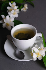 White porcelain cup with fragrant green tea and blooming jasmine on a gray background. Close-up. Time for tea.