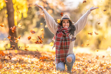 A happy young woman in a park throws leaves during an Indian summer and enjoys autumn