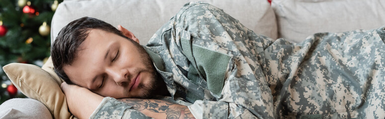 unshaven man in camouflage sleeping on sofa at home, banner