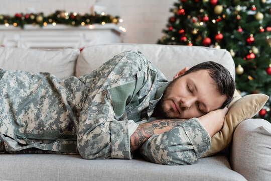 tired bearded man in military uniform sleeping on couch at home on christmas day